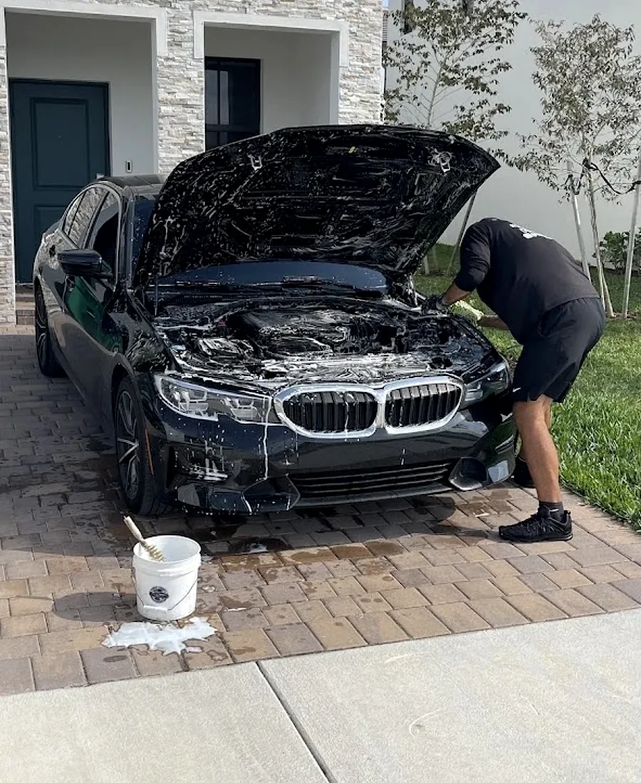 David from Perfect Shine 305 foaming and detailing a BMW engine bay on a brick driveway in Miami